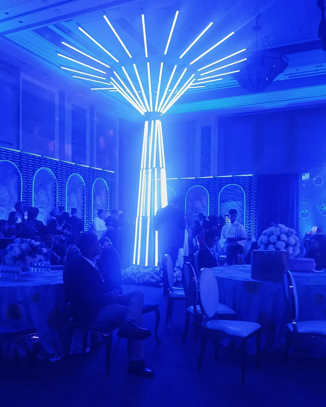 Ballroom ceiling hung with white flowers under blue light