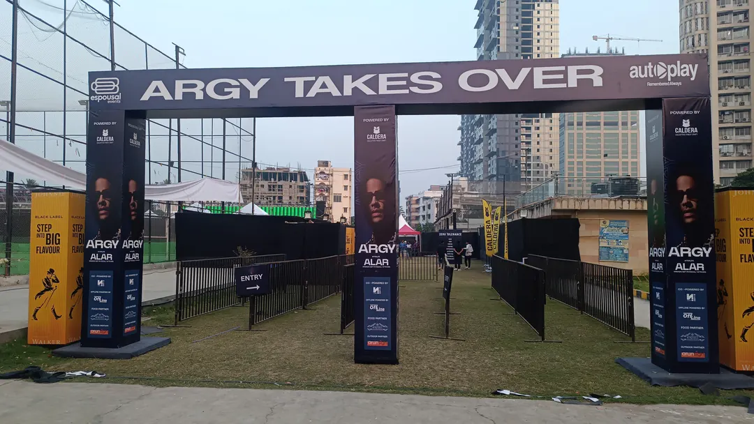 Branded entry arch with queue barriers leading into an outdoor event ground