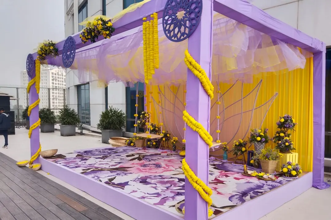 Lilac and marigold haldi canopy with swings and potted flowers on a rooftop deck